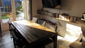 A dining area with a wooden table and chairs, a bookshelf with books, and a TV mounted on the wall. - Fisherman's cottage (Île-d'Arz)