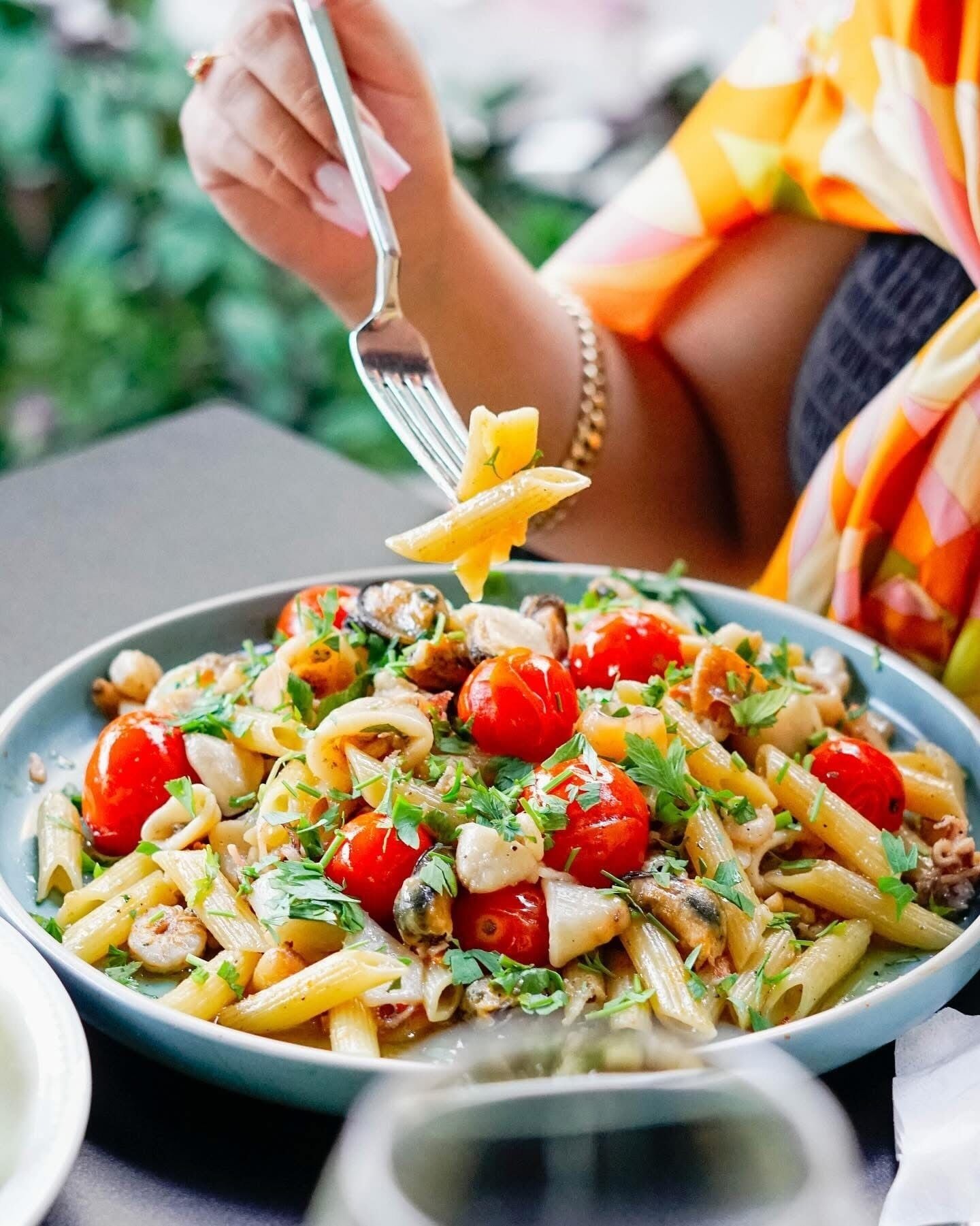 A person serving pasta with cherry tomatoes and herbs.