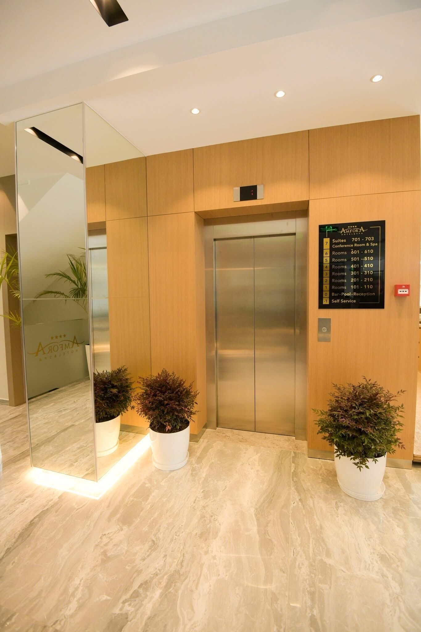 A hotel lobby with a modern elevator, a reception desk, and a directory sign.