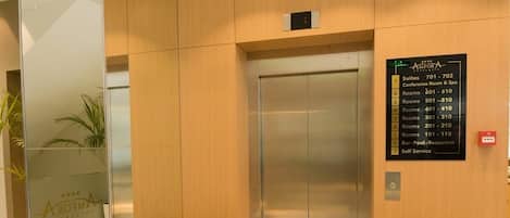 A hotel lobby with a modern elevator, a reception desk, and a directory sign.