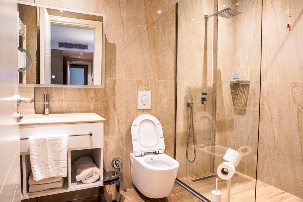 Un baño moderno con ducha envuelta en vidrio, inodoro blanco y tocador con espejo y toallero.