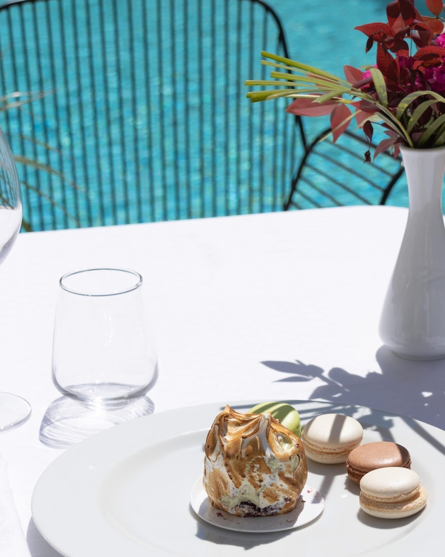 Ein Esstisch mit einer Dessertplatte, einem Glas und einer Vase mit Blumen.