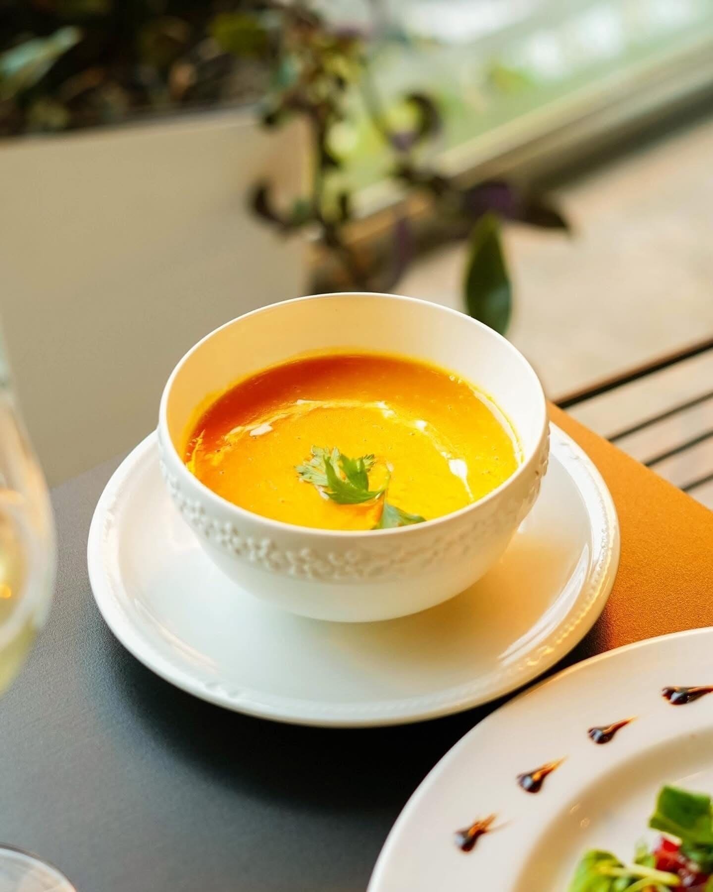 A bowl of soup on a white plate with a saucer, placed on a table.