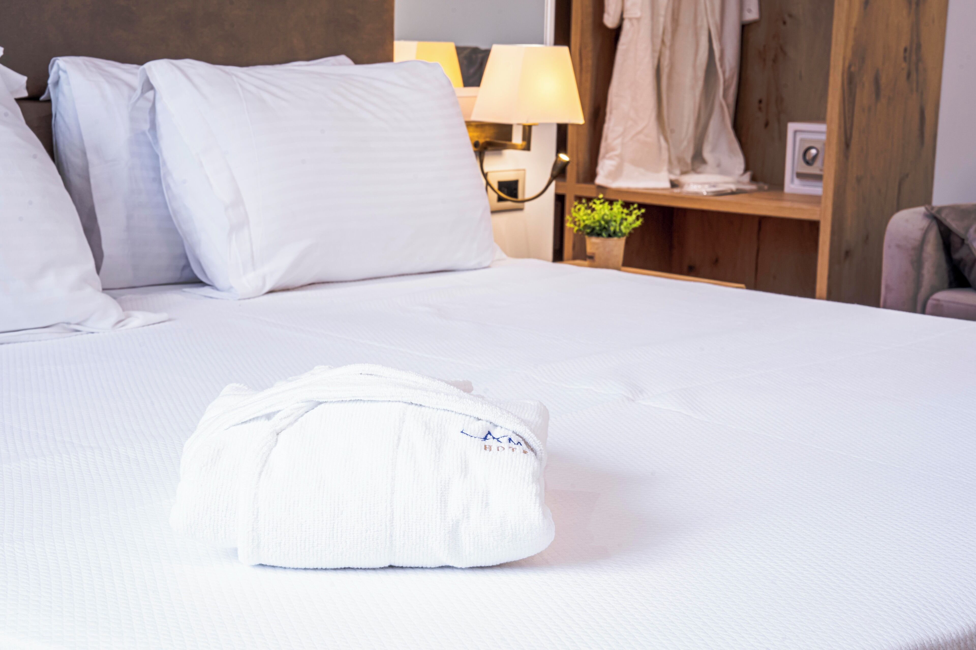 A neatly made bed with white linens, a folded towel, and a lamp on a bedside table.