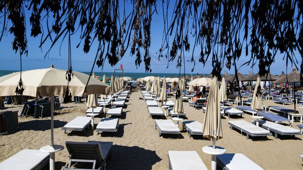 Une plage bordée de rangées de transats et de parasols, dont certains sont occupés.