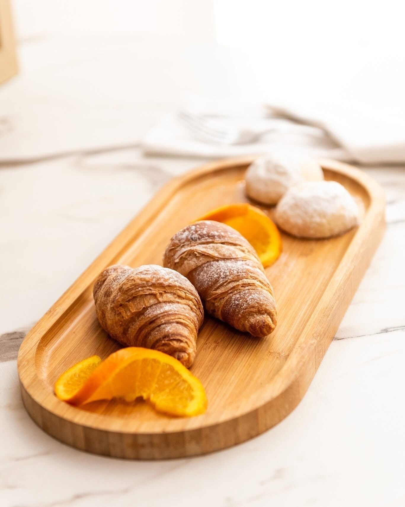 A wooden serving tray with croissants and orange slices on a marble surface.
