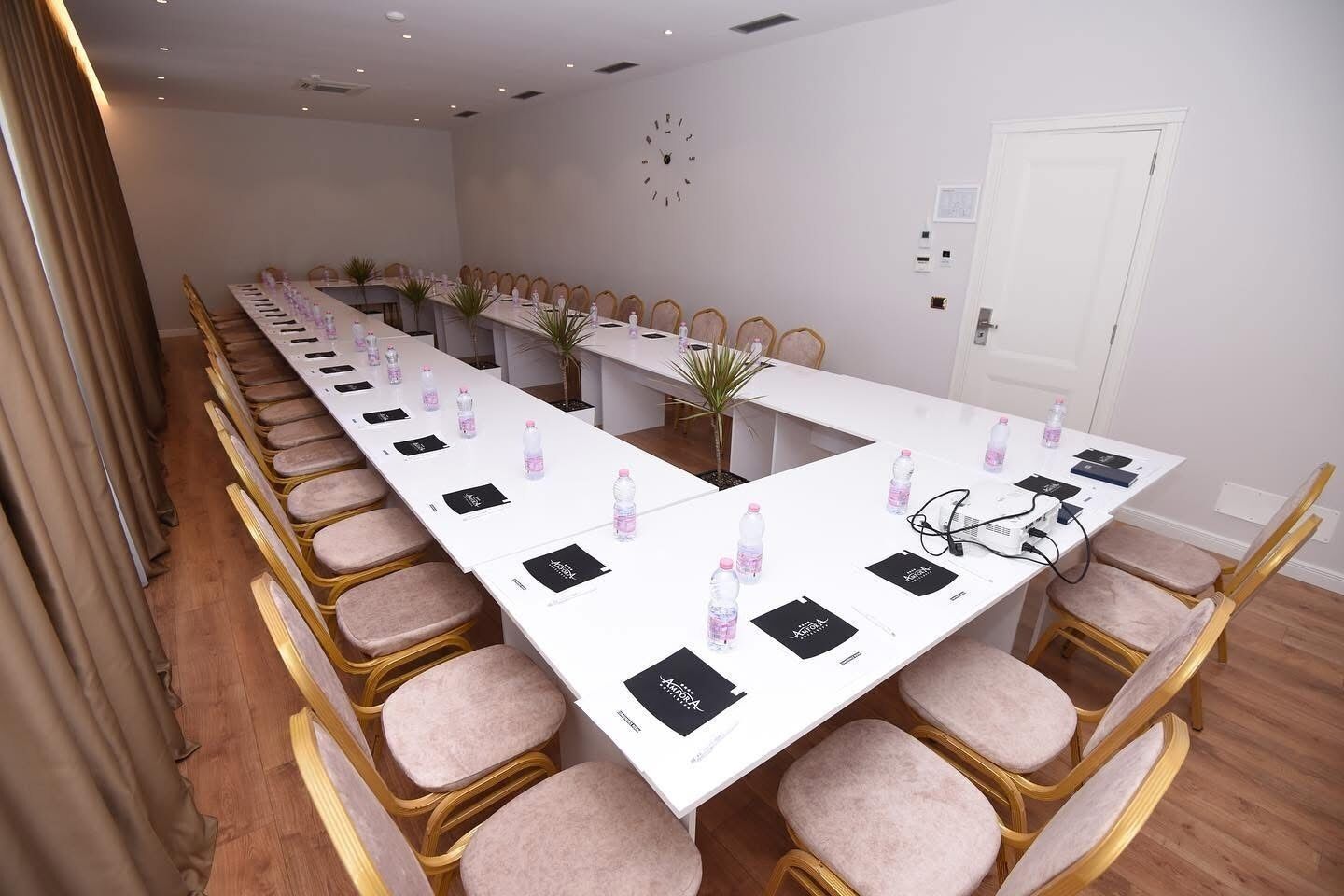 A conference room with a long table, multiple chairs, water bottles, nameplates, and a clock on the wall.