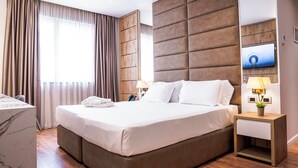 Une chambre d’hôtel moderne avec un grand lit, une tête de lit en bois, une table de chevet avec une lampe et un téléviseur fixé au mur.