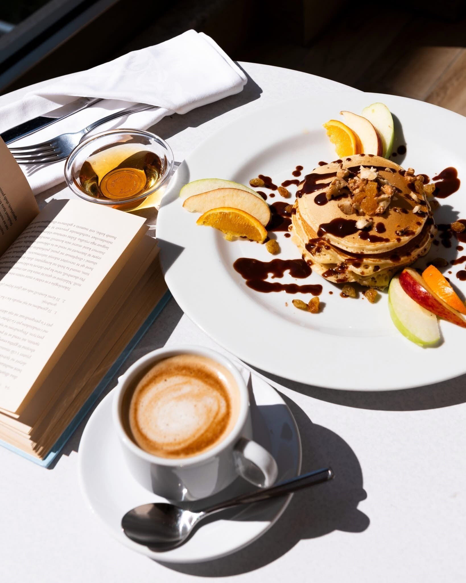 A breakfast setting with pancakes, fruit, and coffee on a table.