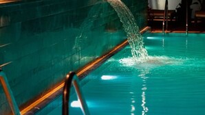 Une piscine agrémentée d’un élément décoratif aquatique, une rambarde en métal et un mur orné de luminaires verticaux.