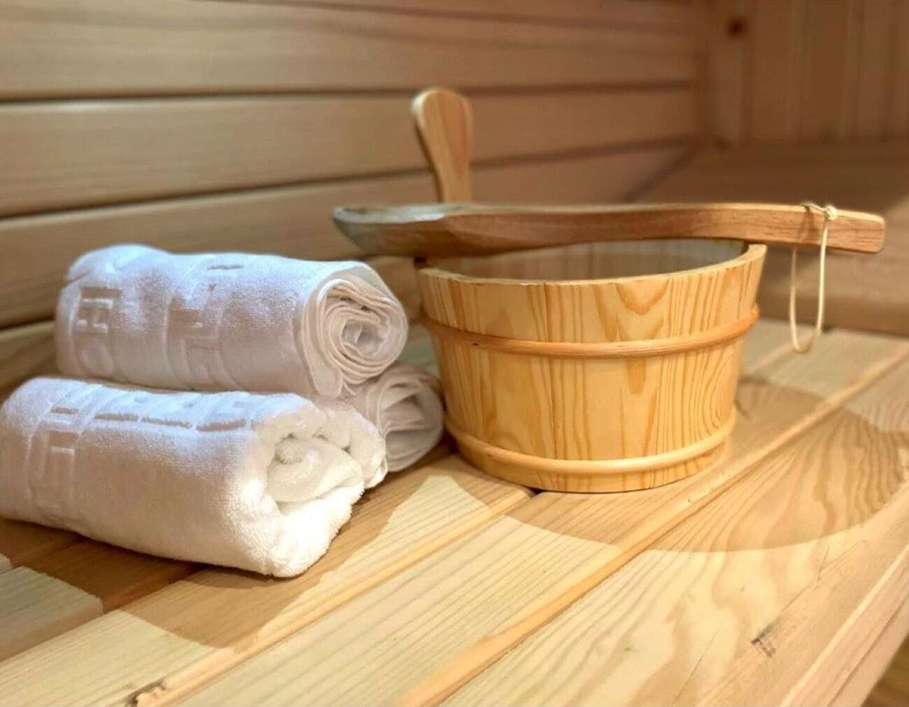 Una sauna con bancos de madera, un cubo de madera y toallas dobladas con cuidado.