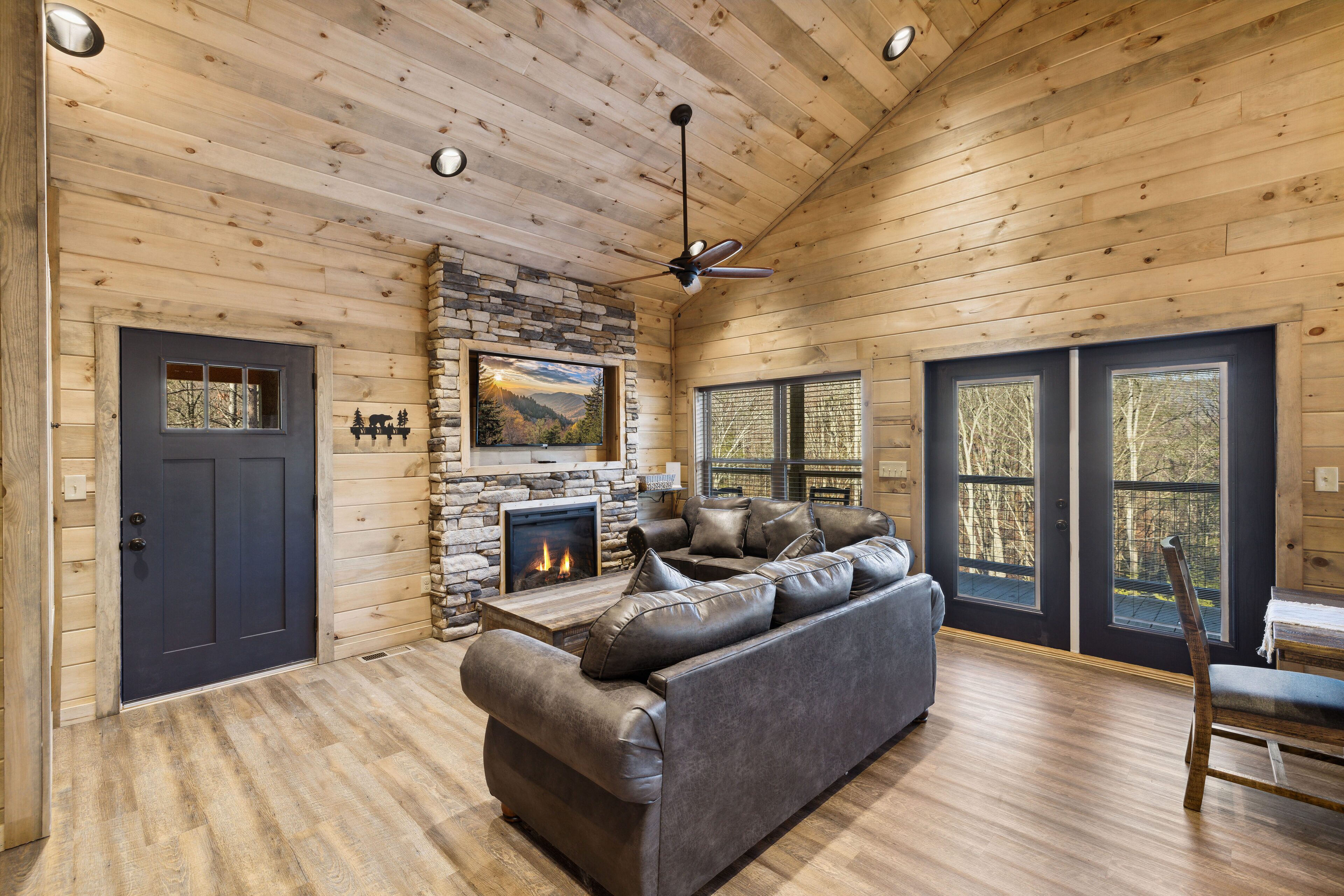Ein Holzblockhaus-Interieur mit Kamin aus Stein, Ledersofa und großen Fenstern.