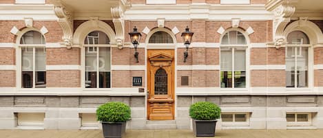 A building with a central wooden door, arched windows, and two potted plants on the ground.