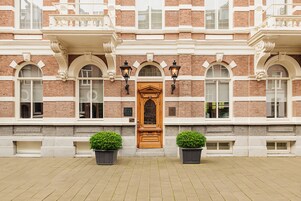 Un edificio con una puerta central de madera, ventanas en arco y dos macetas en el suelo.