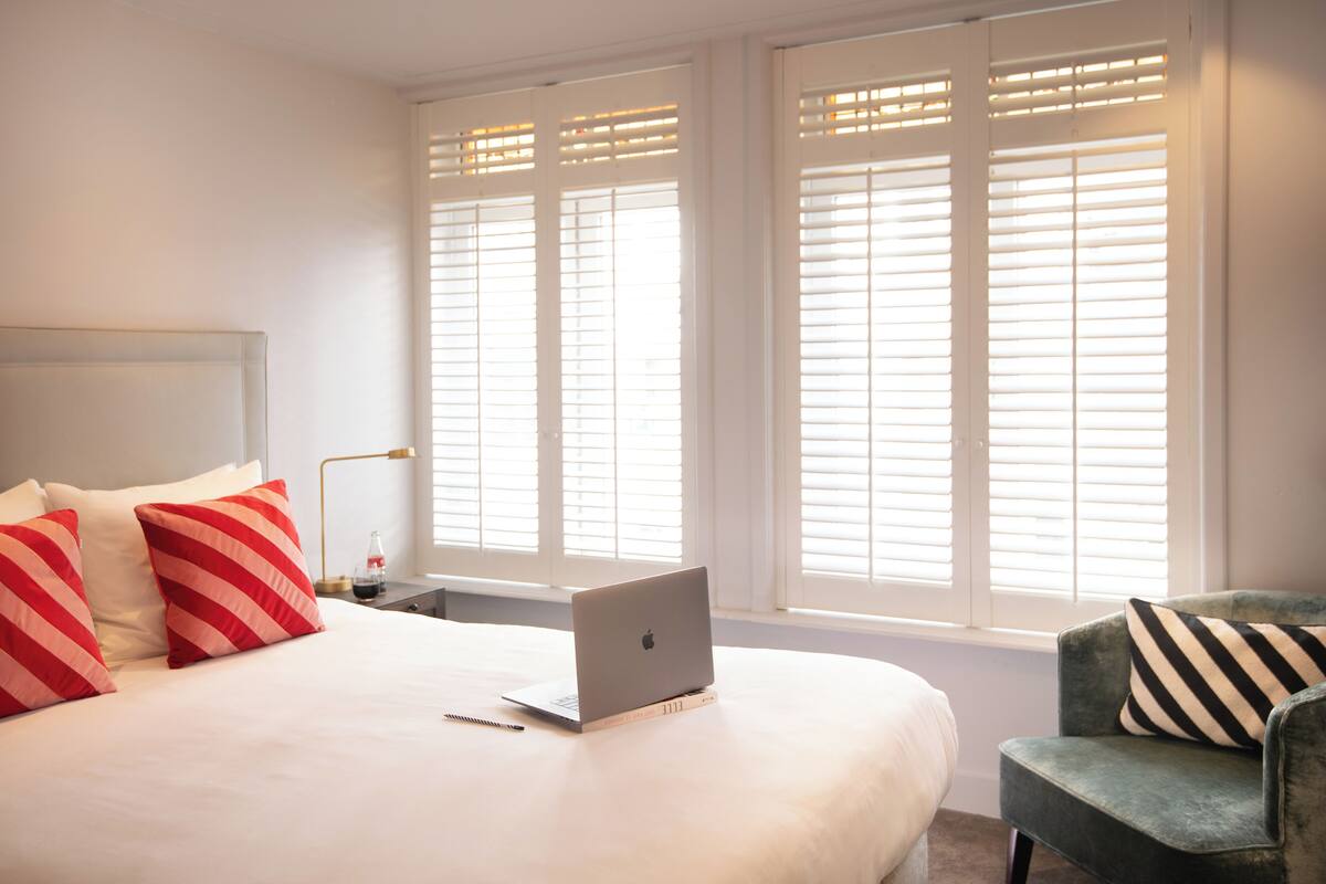 A bedroom with a bed, a laptop on the bed, a chair, and a nightstand with a lamp.