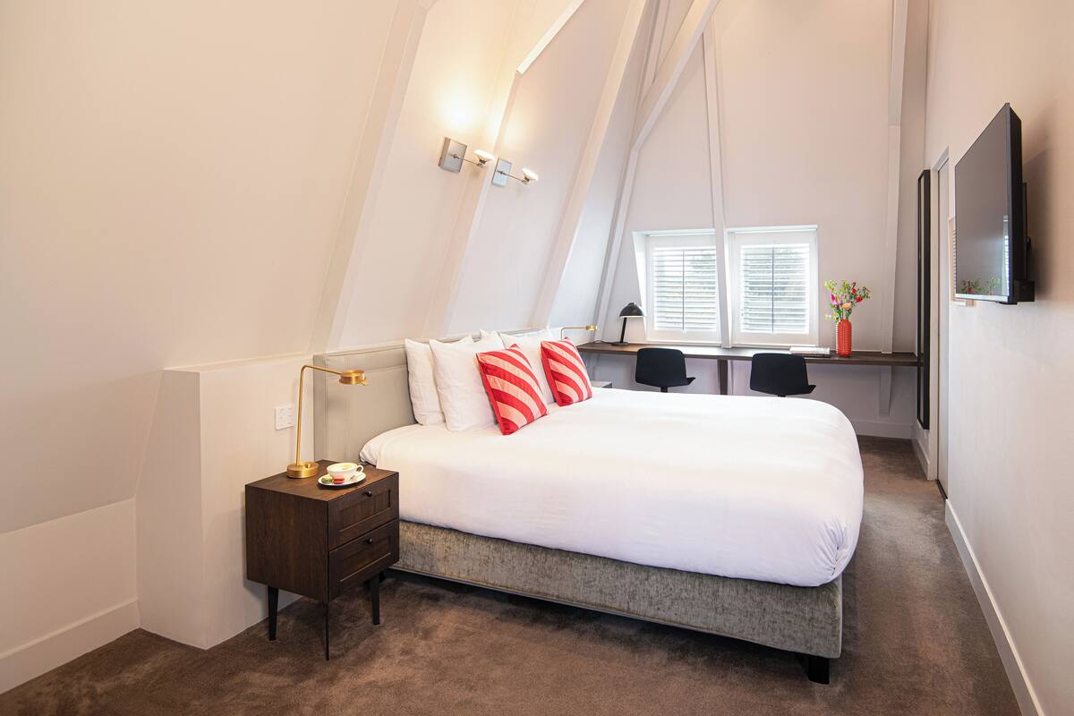 A bedroom with a bed, bedside table, lamp, desk, chairs, and a TV.