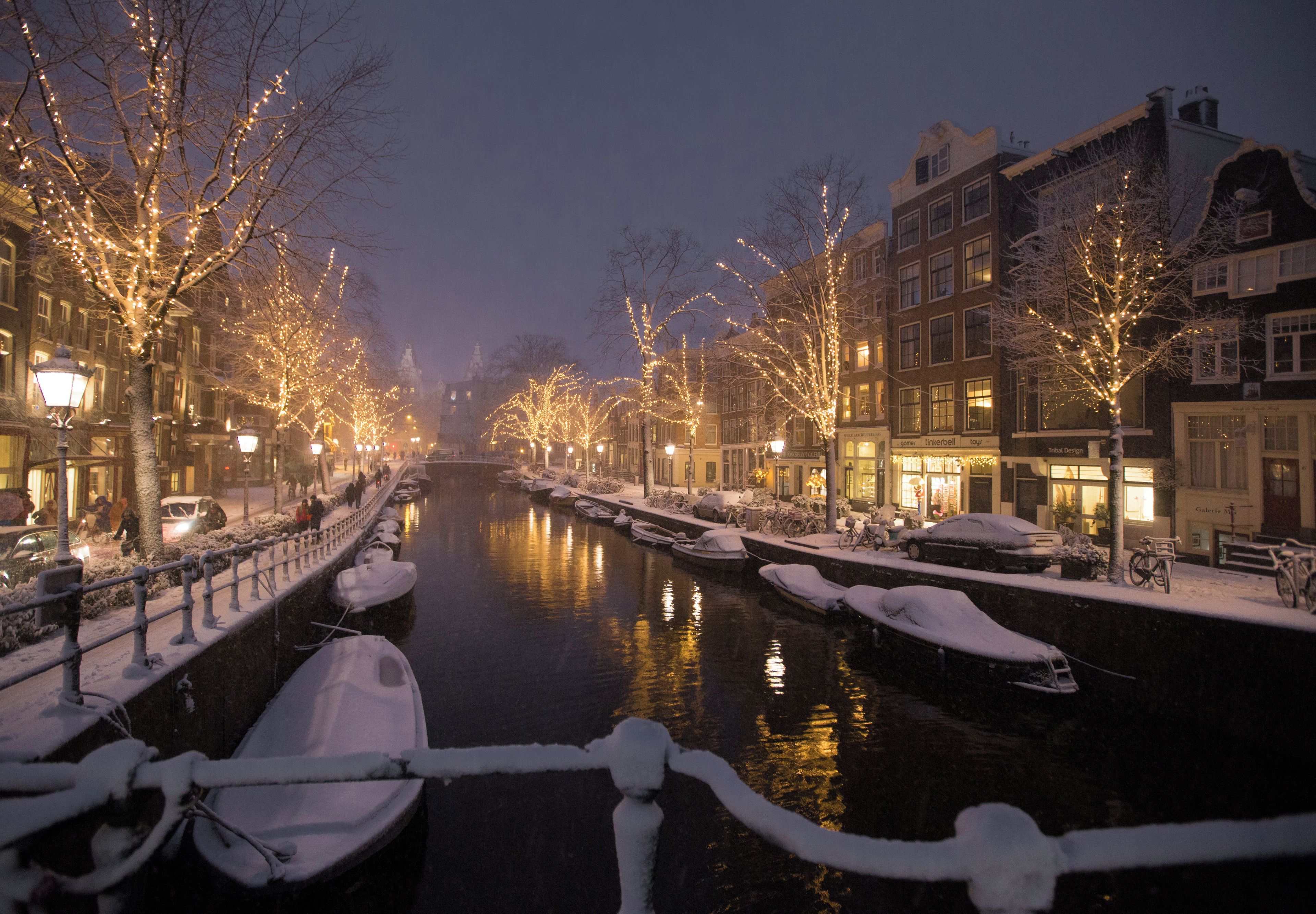 A canal lined with snow-covered trees and buildings, boats docked along the water, and a calm nighttime setting.