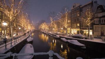 A canal lined with snow-covered trees and buildings, boats docked along the water, and a calm nighttime setting.