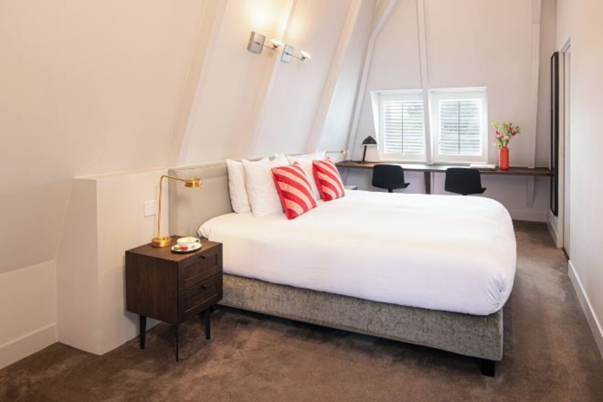 A bedroom with a bed, nightstand, desk, and window with blinds.