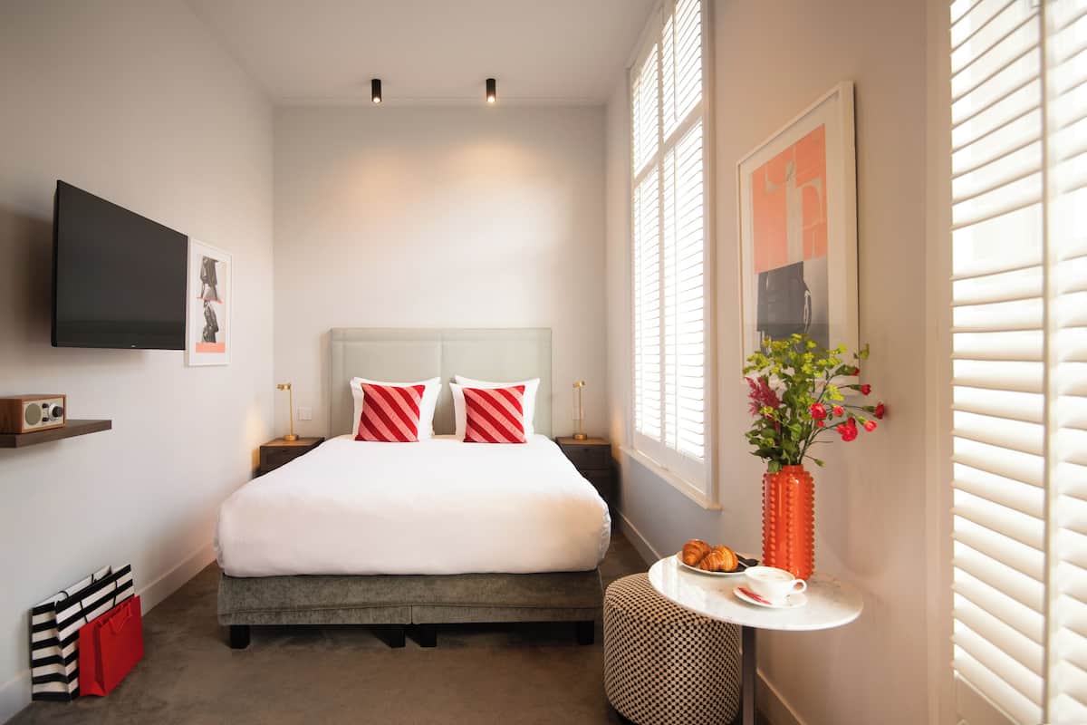 A neatly arranged bedroom with a bed, bedside tables, a TV, and a small table with a vase and pastries.