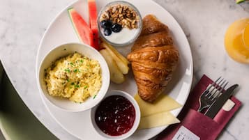 Un plato de desayuno con huevos revueltos, un croissant, fruta, yogur y granola.