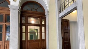 Uma entrada imponente com uma grande porta de madeira, uma escadaria e uma janela em arco.