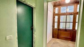 Um corredor com uma porta verde, uma porta de madeira com painéis de vidro e piso de azulejos.