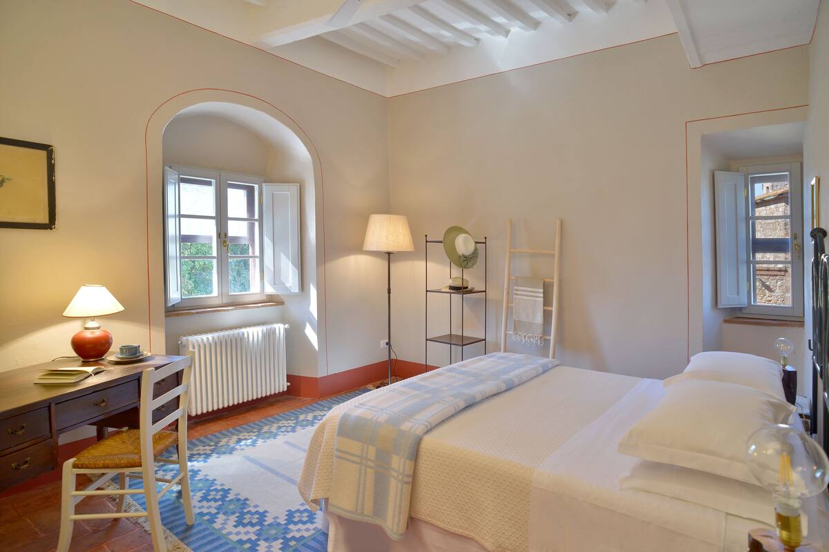 A bedroom with a bed, a desk, a chair, a radiator, and a window.