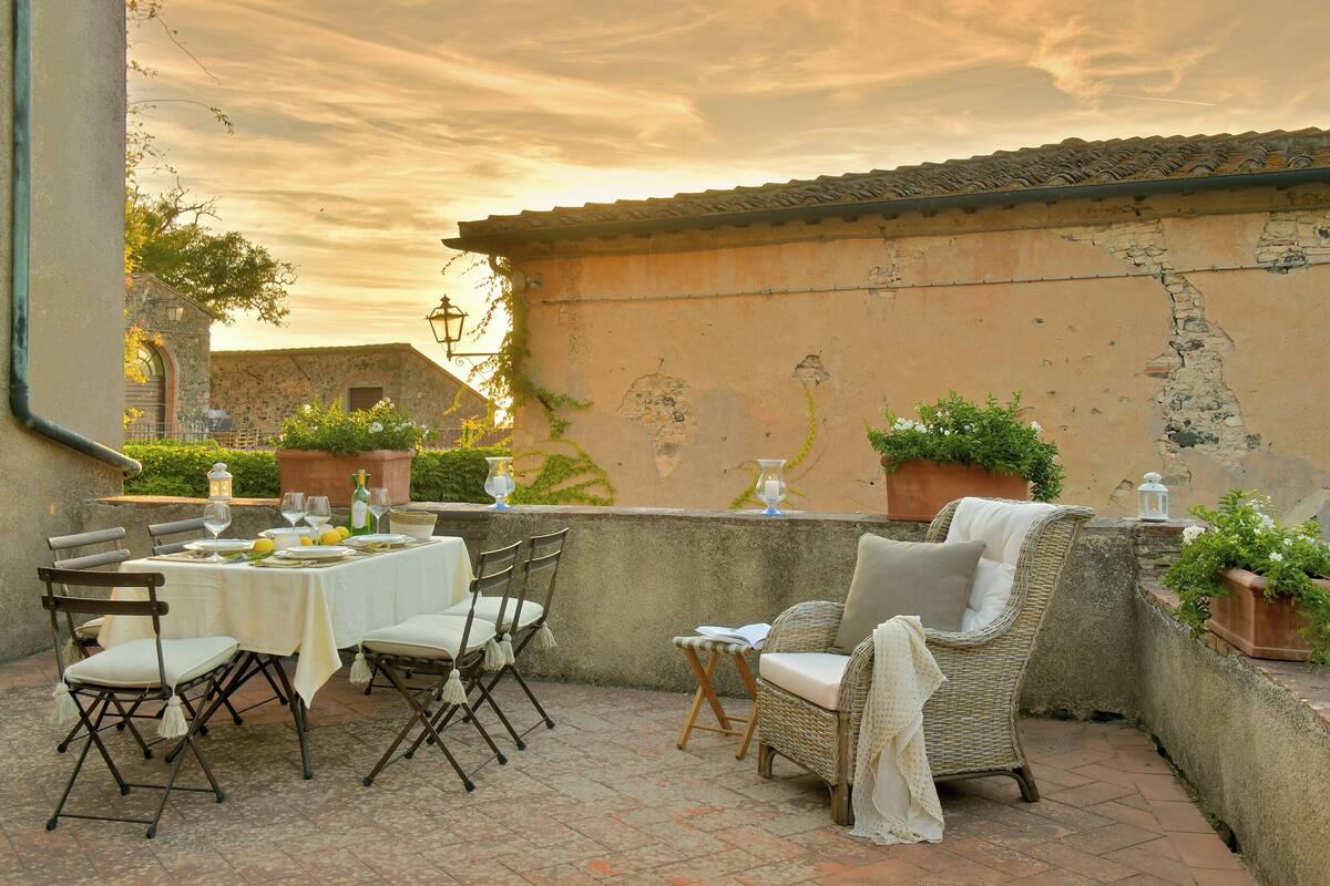 An outdoor patio with a table set for dining, wicker chairs, and potted plants.