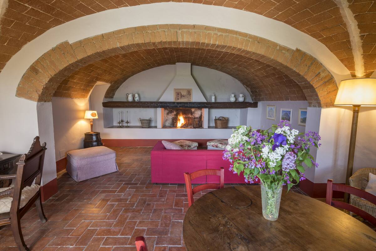 A cozy room with a brick fireplace, a wooden table, and a bench.