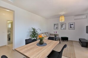 Een moderne eetruimte met een houten tafel, zwarte stoelen, een vaas met bloemen, een geweven hanglamp en een bank met kussens.