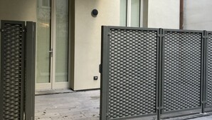 A metal gate with a diamond plate pattern, a door with a glass panel, and a building facade with a textured surface. - Il Bosco Segreto, where magic and history come together (Torino)