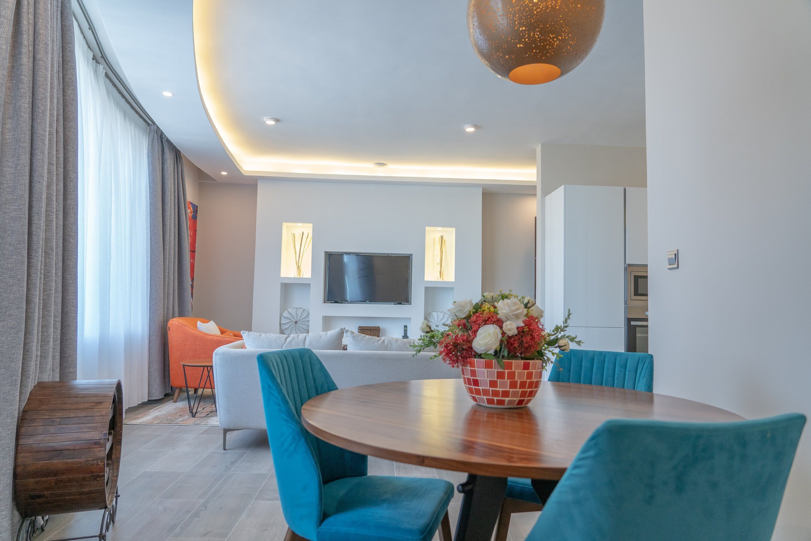 A modern living room with a round wooden table, teal chairs, and a floral centerpiece.