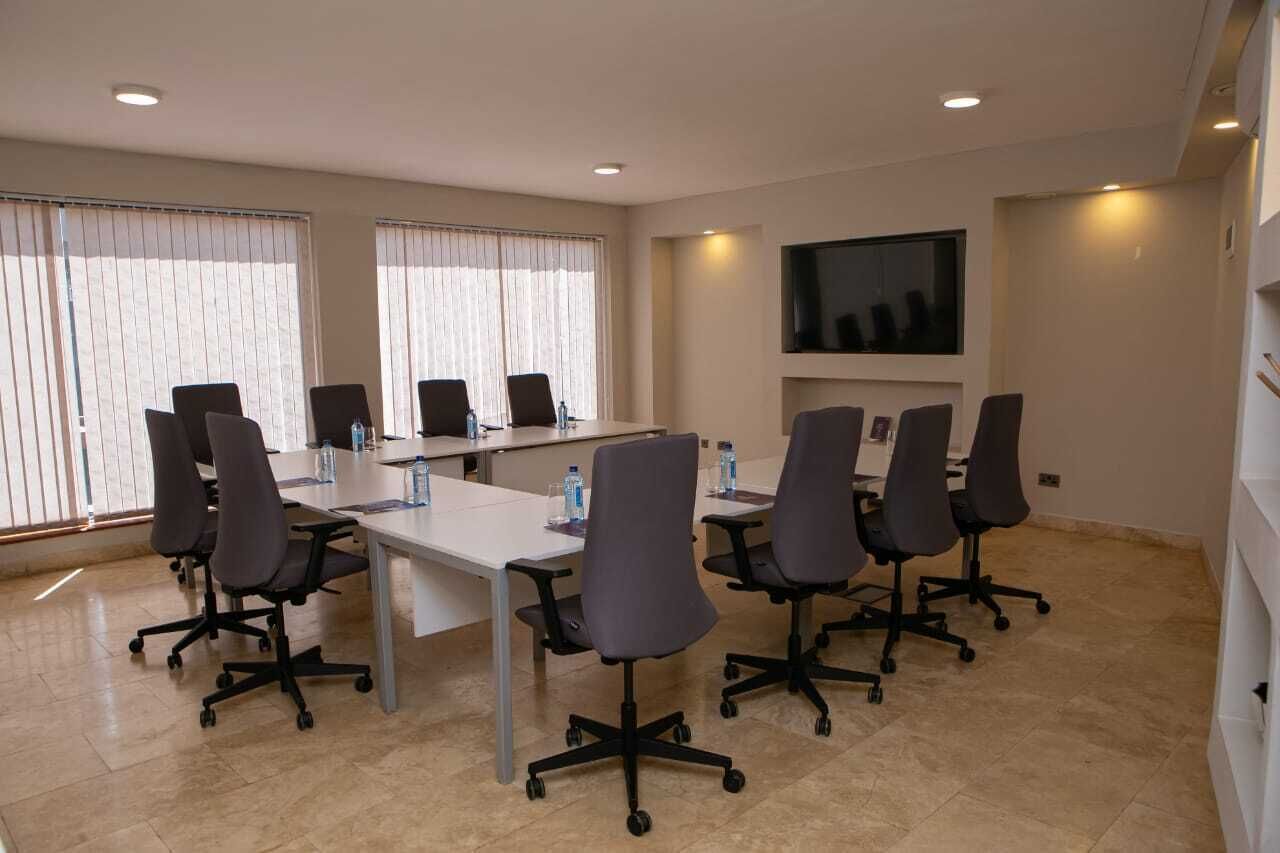 A conference room with a long table, six chairs, and a flat-screen TV on the wall.