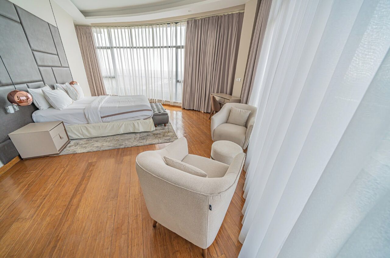 Una habitación de hotel moderna con cama, sofá, escritorio y un ventanal con cortinas.