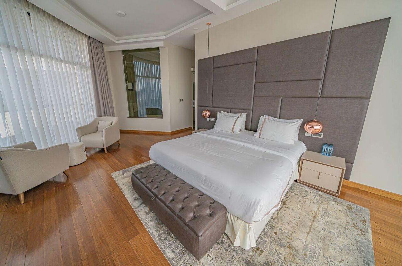 A modern bedroom with a large bed, a tufted bench, a bedside table, and a chair.