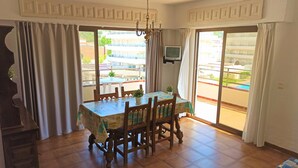 A dining area with a wooden table and chairs, a chandelier, and a television on the wall. - Estartit Trill EOLO (L'Estartit)