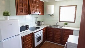 A compact kitchen with wooden cabinets, a built-in oven, a refrigerator, a sink, and a window. - Estartit Trill EOLO (L'Estartit)