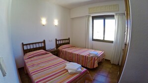 A room with two beds, each with striped bedding, a window with curtains, and a wall-mounted light fixture. - Estartit Trill EOLO (L'Estartit)