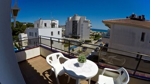 A balcony with white plastic chairs and a small table, overlooking a residential area with buildings and a clear blue sky. - Estartit Trill EOLO (L'Estartit)