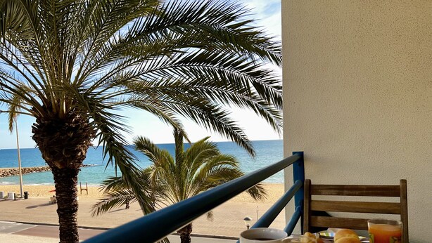 Ein Balkon mit Frühstückstisch, mit Blick auf einen Strand und das Meer.
