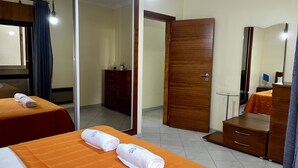 Ein Hotelzimmer mit zwei Betten, einem Holzschrank, einem Spiegel und einem kleinen Schreibtisch mit Stuhl.