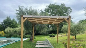 A wooden pergola structure in a garden with a pool and various plants.