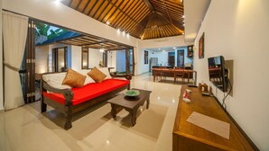 A spacious living area with a wooden ceiling, a red sofa, a coffee table, and a TV on the wall.