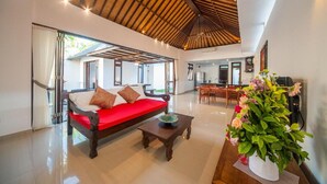 A spacious living area with a red sofa, wooden coffee table, and a large potted plant.