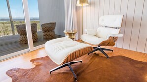 Een moderne kamer met een groot raam, een witte stoel, een vloerlamp en een kleden van koeienhuid.