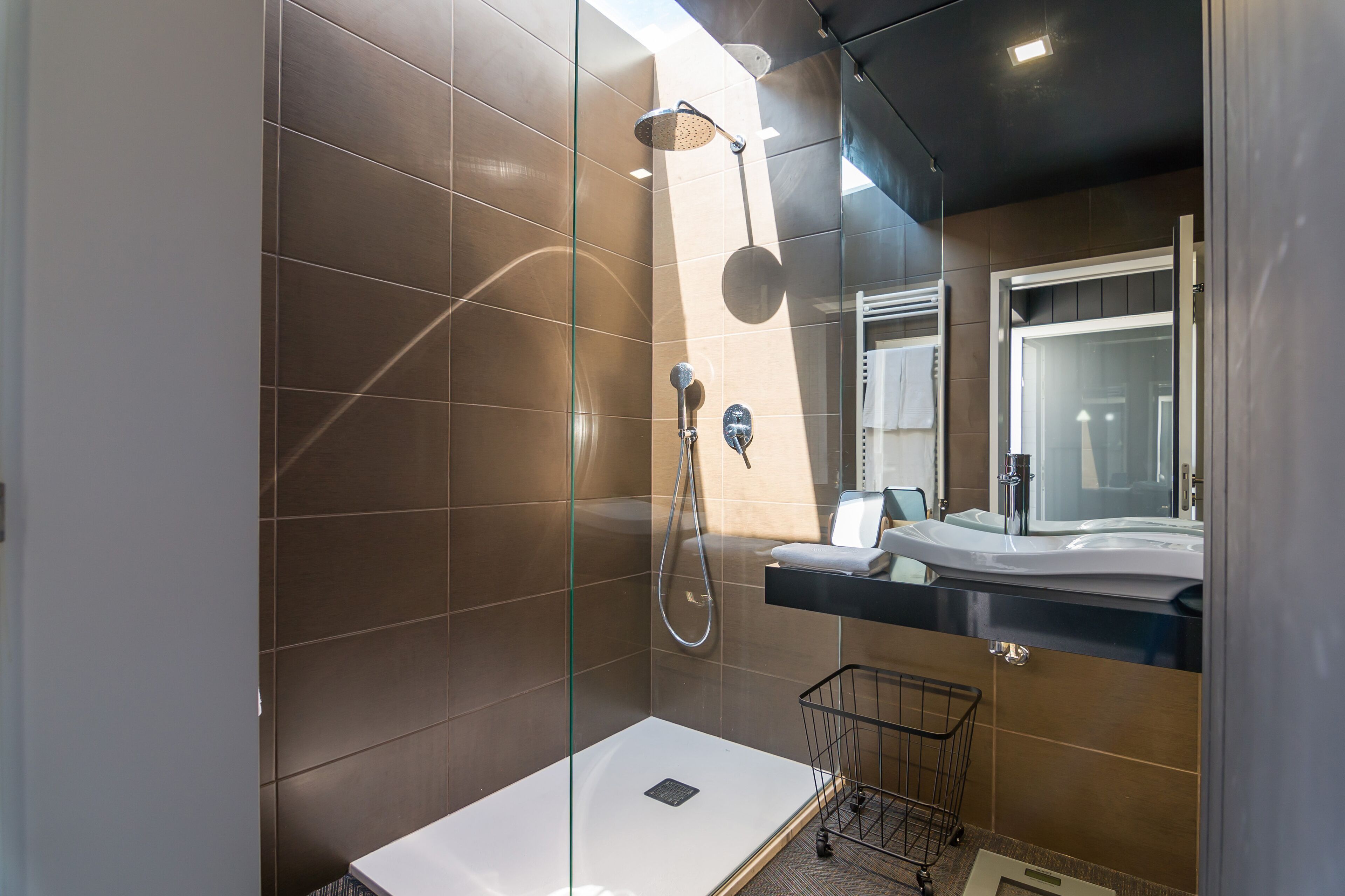 Un baño moderno con cabina de ducha de vidrio, tocador con espejo y un lavamanos pequeño.