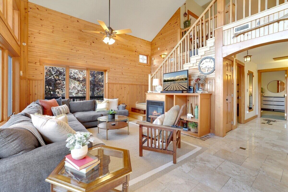 A spacious living room with a large sofa, a fireplace, and a wooden staircase.