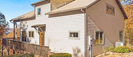 A two-story white building with a sloped roof, a wooden deck, and a small porch.