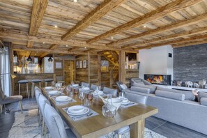 A modern interior with a wooden ceiling, a dining area with a long table set for six, and a cozy seating area with a fireplace.